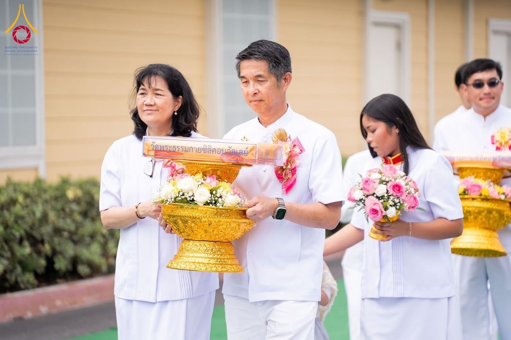 กลุ่มคนในชุดสีขาวถือพานพุ่มดอกไม้และผ้าไตรในพิธีทางศาสนา
