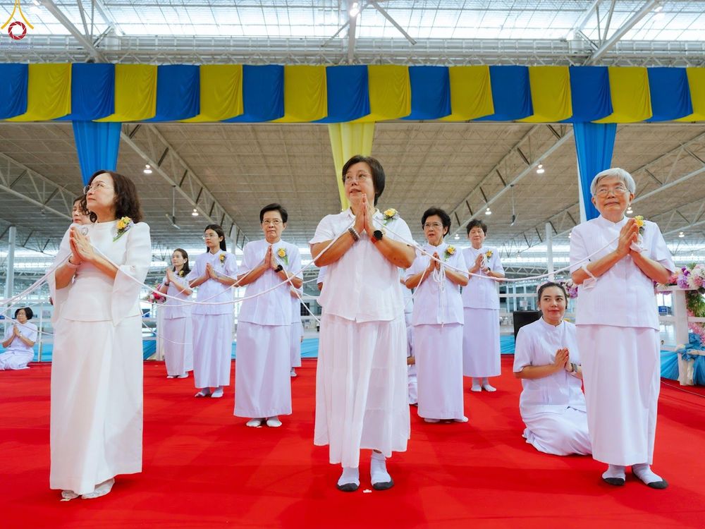 กลุ่มสาธุชนหญิงสวมชุดขาวพนมมือถือสายสิญจน์ในพิธีทางศาสนาบนพรมสีแดง