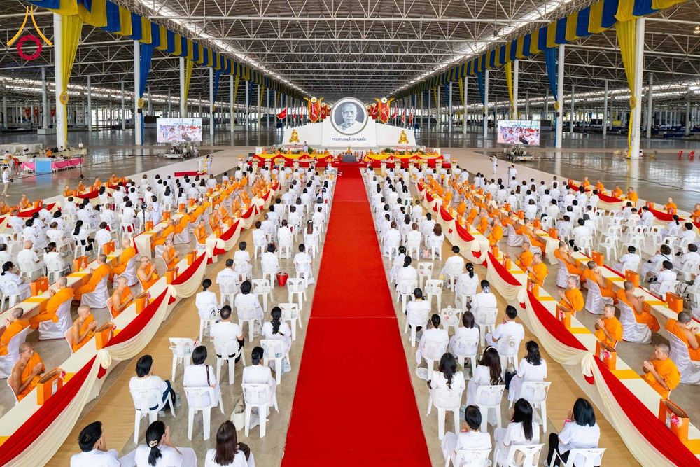 มุมมองมุมสูงภายในสภาธรรมกายสากลที่มีผู้เข้าร่วมพิธีนั่งบนเก้าอี้เรียงรายเป็นระเบียบสองฝั่งทางเดินพรมสีแดง