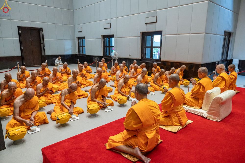 พระภิกษุสงฆ์จำนวนมากในจีวรสีเหลืองทองกำลังนั่งประกอบศาสนกิจภายในอาคาร
