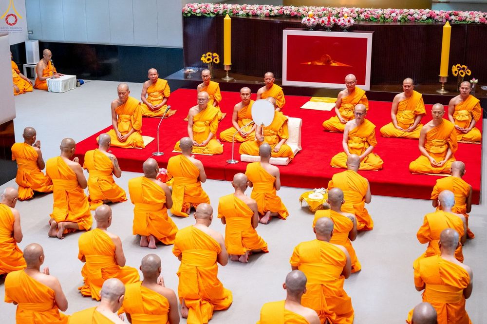 กลุ่มพระภิกษุและสามเณรนั่งพนมมือในพิธีอุปสมบทหมู่ภายในอาคาร