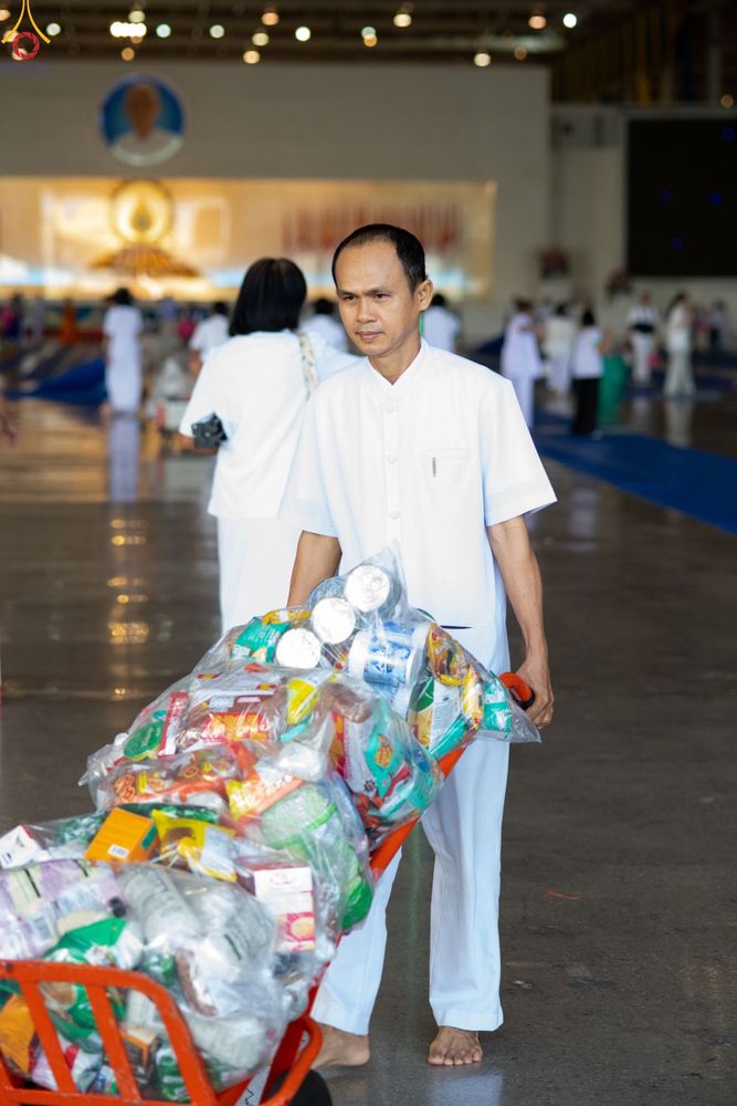ชายสวมชุดสีขาวกำลังเข็นรถเข็นที่เต็มไปด้วยถุงข้าวสารอาหารแห้งภายในโถงอาคาร