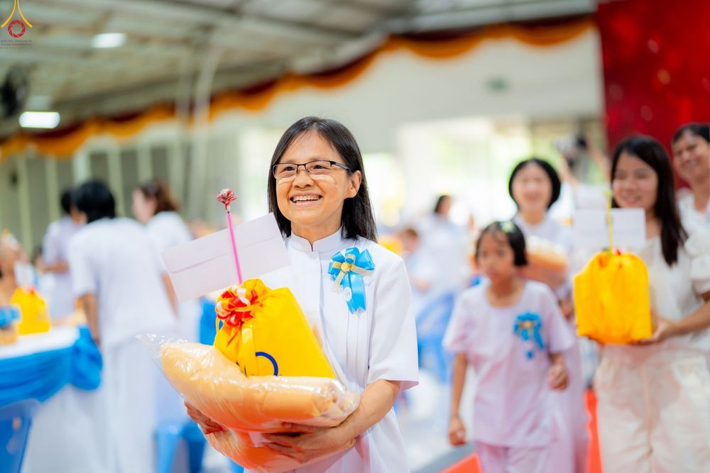 หญิงสวมชุดขาวถือชุดสังฆทานสีเหลืองยิ้มแย้มในงานบุญ