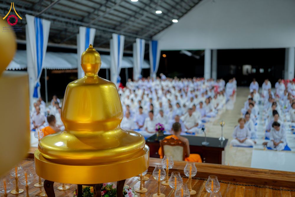 พระพุทธรูปจำลองสีทองตั้งอยู่หน้ากลุ่มผู้เข้าร่วมโครงการอบรมในชุดสีขาวภายในอาคาร