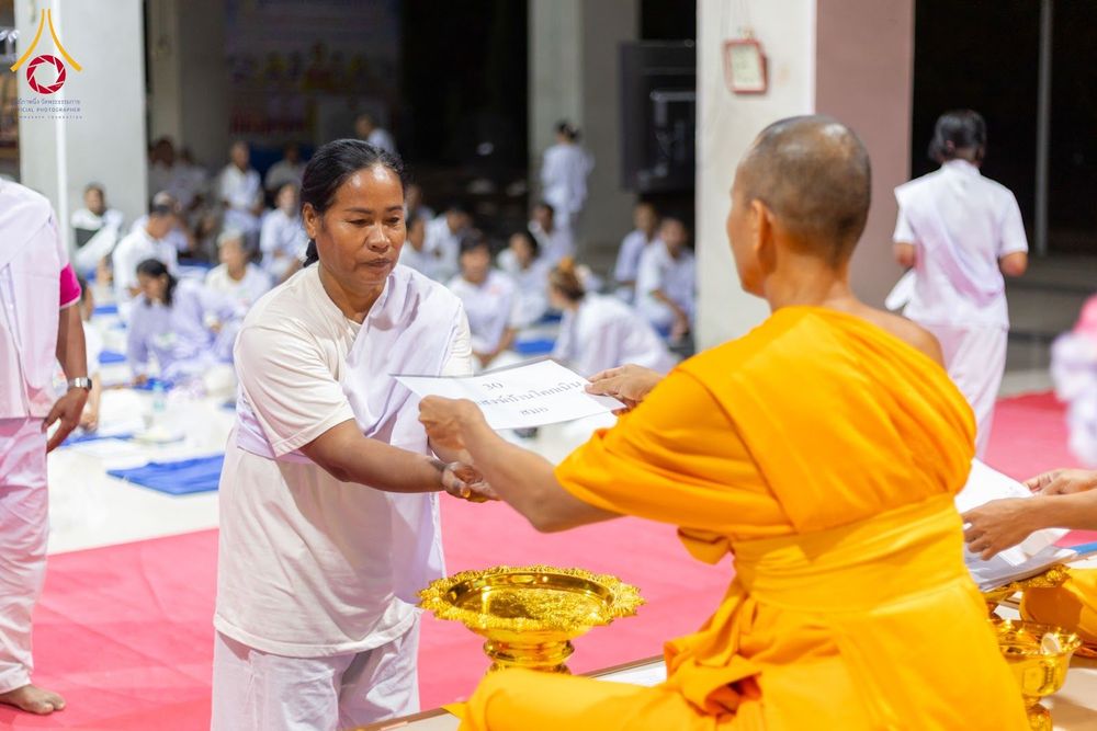 อุบาสิกาสวมชุดสีขาวกำลังรับเอกสารจากพระภิกษุสงฆ์ในพิธีอบรม