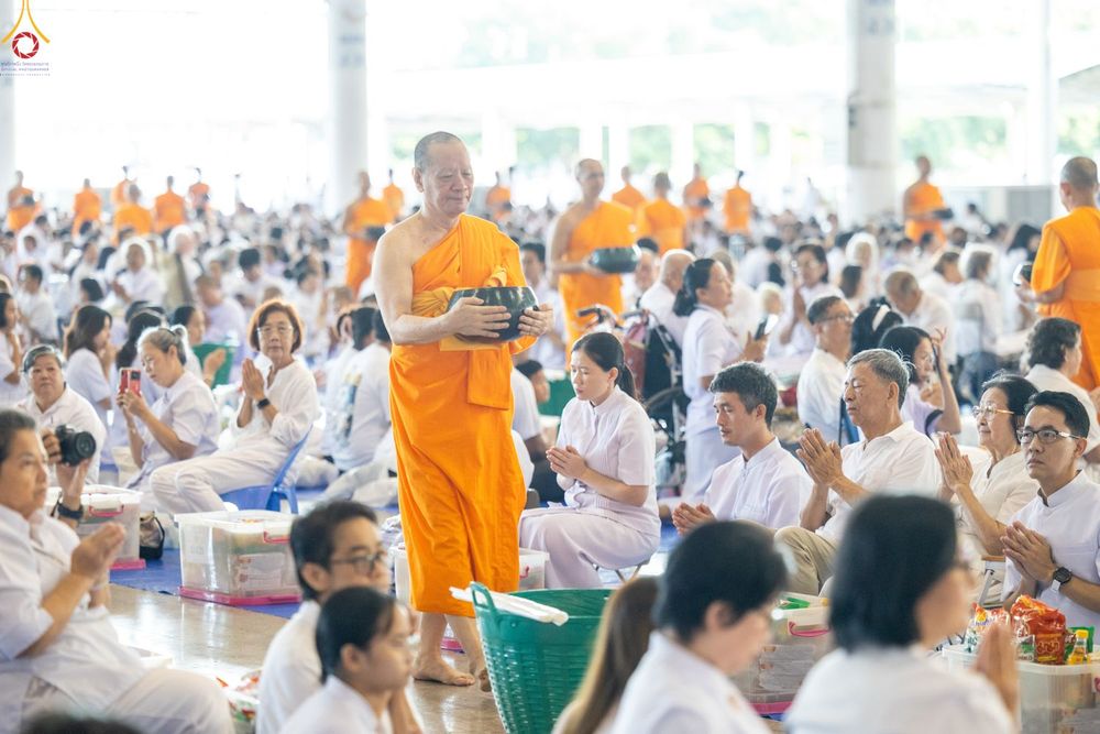พระภิกษุสงฆ์เดินรับบิณฑบาตจากพุทธศาสนิกชนชุดขาวภายในอาคารขนาดใหญ่