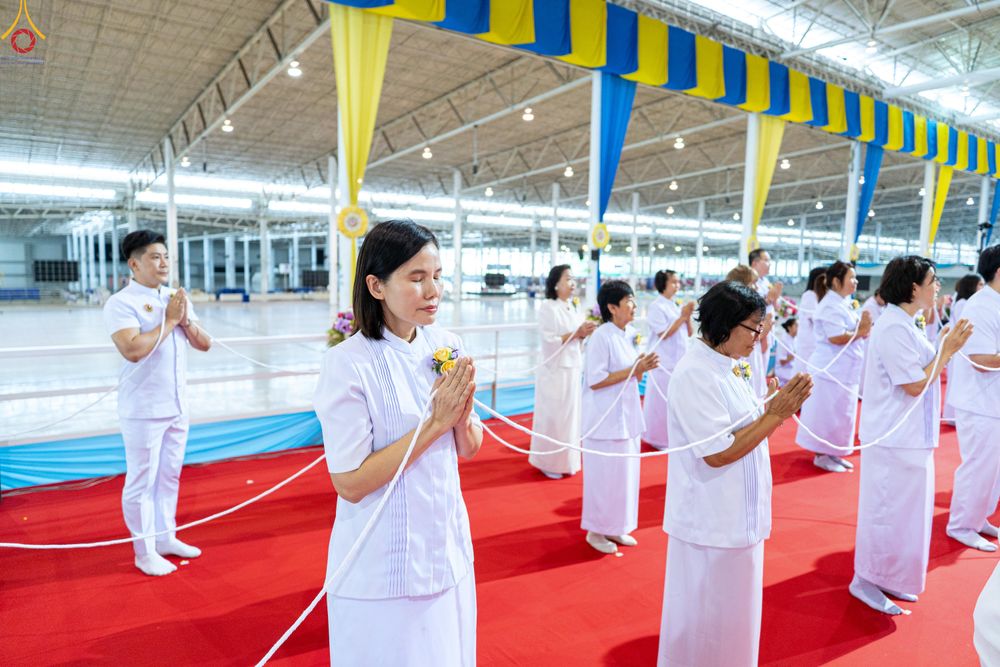 กลุ่มคนสวมชุดขาวพนมมือถือสายสิญจน์ในพิธีทางศาสนาภายในอาคาร