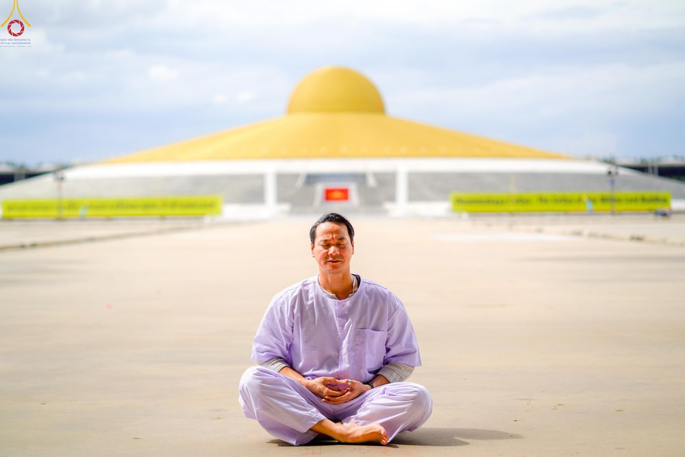 ชายชาวต่างชาตินั่งสมาธิอยู่บนลานกว้างโดยมีมหาธรรมกายเจดีย์สีทองเป็นฉากหลัง