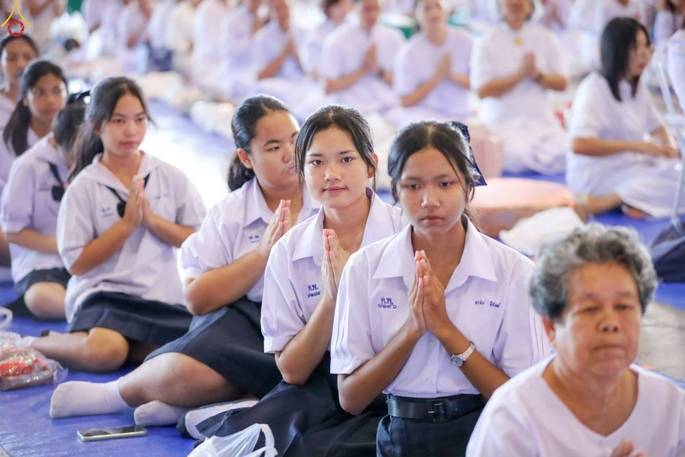 นักเรียนหญิงหลายคนสวมชุดนักเรียนนั่งพนมมือด้วยความสงบในพิธีทางศาสนา
