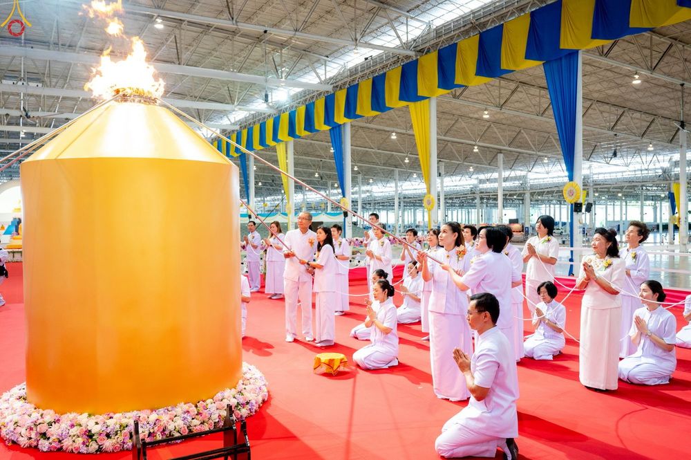 กลุ่มคนในชุดขาวกำลังประกอบพิธีจุดเทียนใจ ไฟนิรันดร์ อนันตชัย โดยมีโคมไฟสีทองขนาดใหญ่อยู่ด้านหน้า