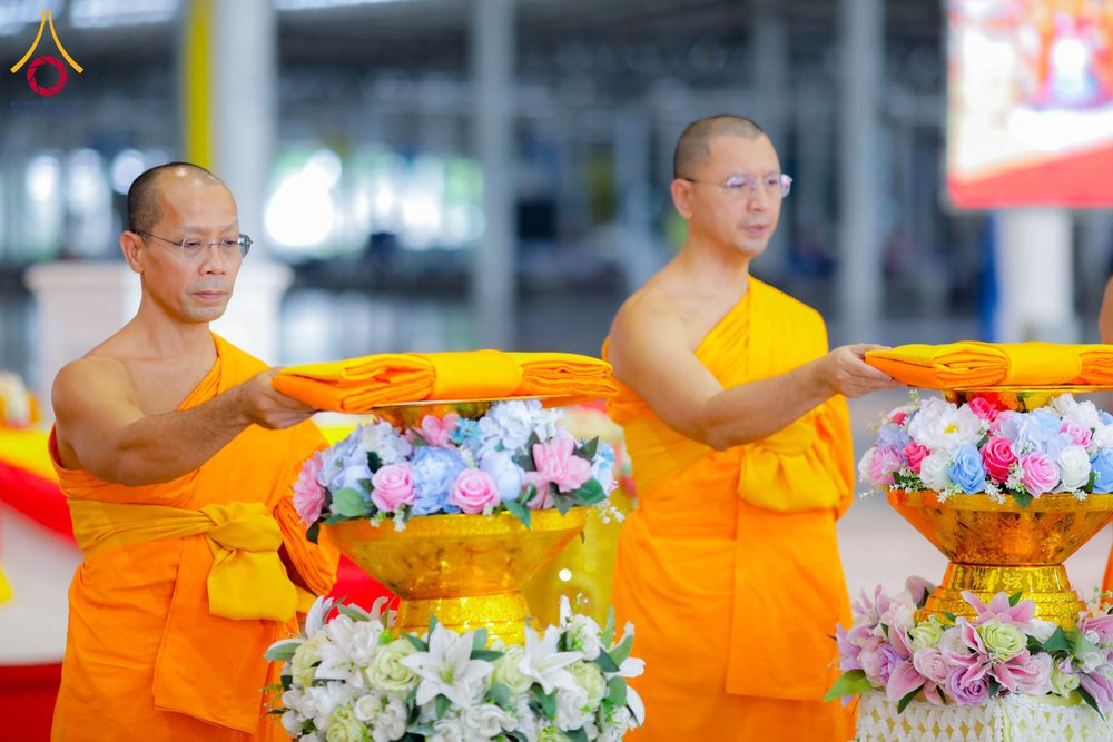 พระภิกษุสองรูปกำลังถือพานพุ่มดอกไม้ที่มีผ้าไตรวางอยู่เพื่อประกอบพิธีทางศาสนา