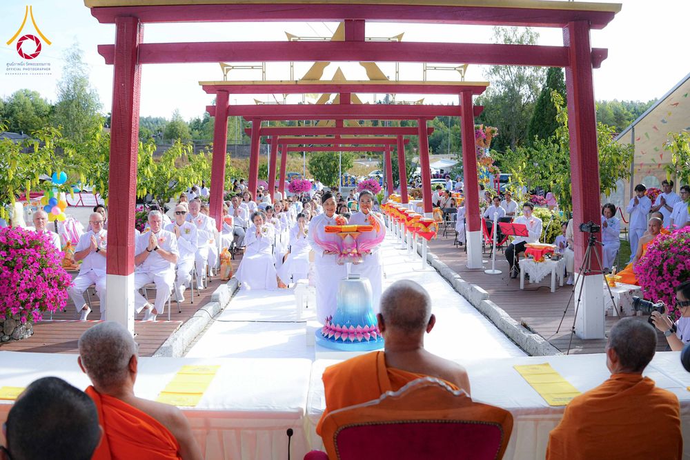 พุทธศาสนิกชนชุดขาวร่วมพิธีทอดผ้าป่าสามัคคีภายใต้ซุ้มประตูสีแดง โดยมีพระภิกษุสงฆ์เป็นประธานในพิธี