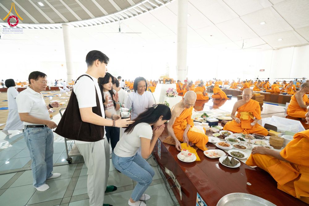 กลุ่มพุทธศาสนิกชนกำลังถวายภัตตาหารแด่พระภิกษุสงฆ์ภายในอาคารหอฉัน