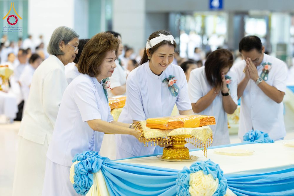 กลุ่มพุทธศาสนิกชนในชุดขาวกำลังร่วมพิธีทอดผ้าป่า โดยมีผู้หญิงสองคนกำลังประคองพานพุ่มที่มีผ้าไตรจีวรวางอยู่