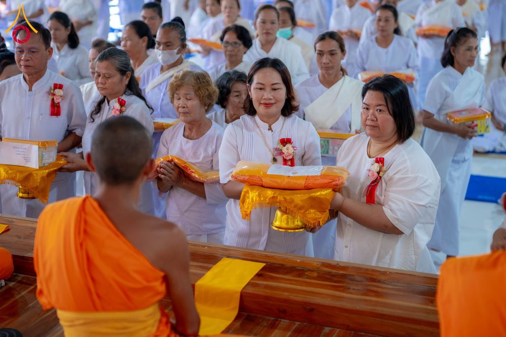 กลุ่มอุบาสิกาแก้วสวมชุดสีขาวกำลังถือพานถวายผ้าไตรแด่พระภิกษุสงฆ์ในพิธีทางศาสนา