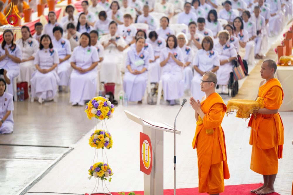 พระภิกษุสงฆ์กำลังประกอบพิธีกรรมทางศาสนาต่อหน้าสาธุชนที่สวมชุดขาวจำนวนมากภายในอาคาร