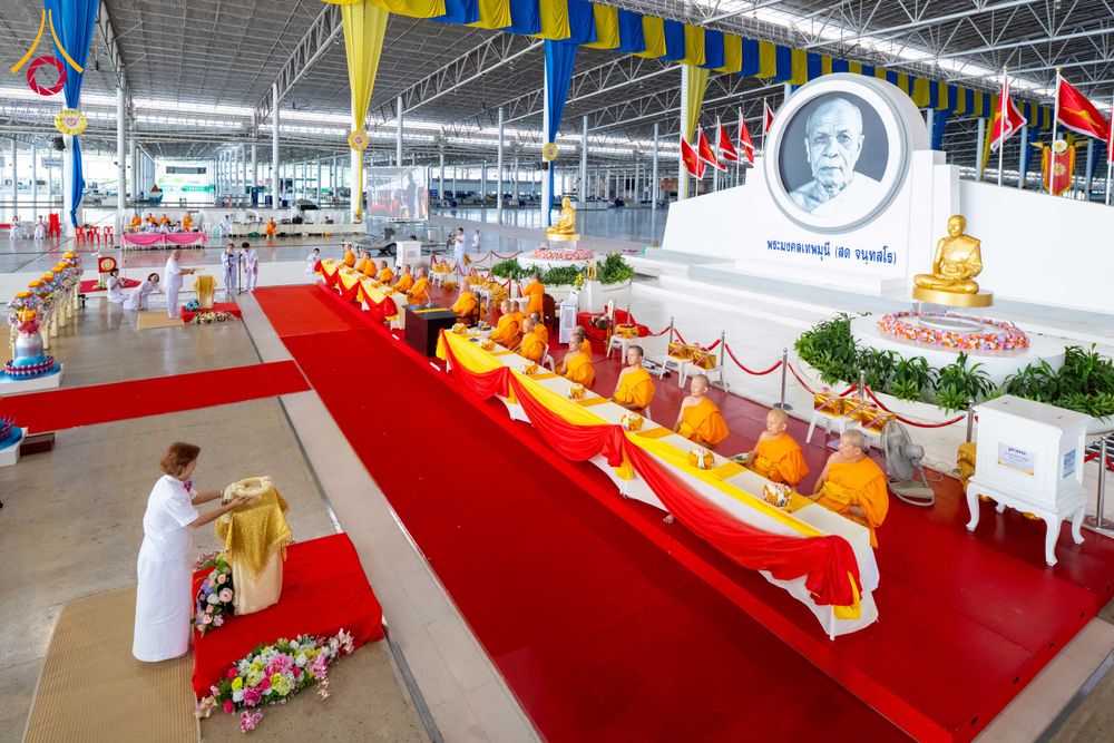 พระภิกษุสงฆ์นั่งเรียงแถวบนอาสนะเพื่อรับถวายมหาสังฆทานภายในอาคารขนาดใหญ่ที่มีพุทธศาสนิกชนชุดขาวร่วมพิธี