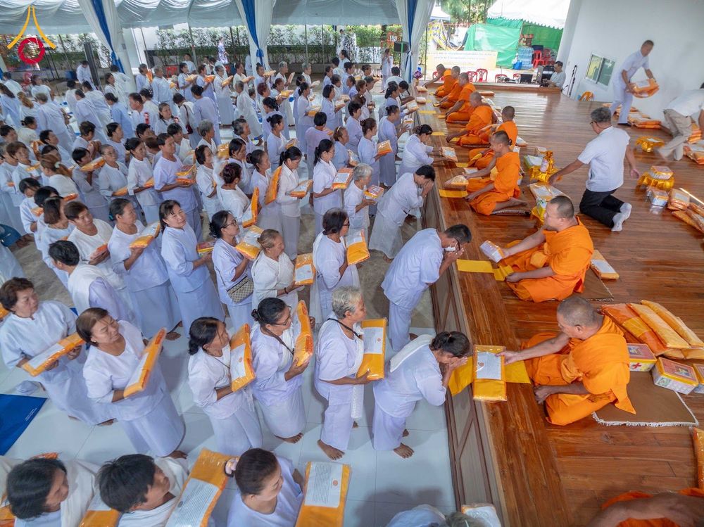 กลุ่มอุบาสิกาชุดขาวกำลังเข้าแถวถวายสังฆทานแด่พระภิกษุสงฆ์ที่นั่งอยู่บนอาสนะไม้