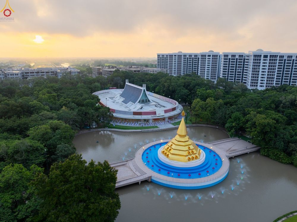 มุมสูงของโบสถ์พระไตรปิฎกและเจดีย์สีทองกลางน้ำท่ามกลางต้นไม้และอาคารในช่วงเช้า