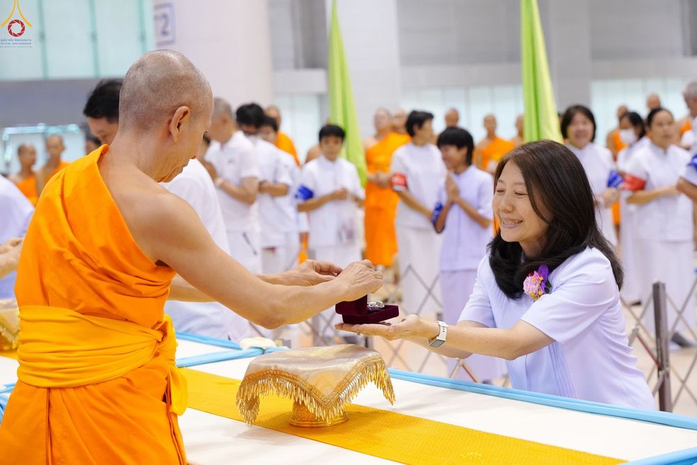 พระภิกษุกำลังส่งมอบพระของขวัญให้แก่หญิงสาวในชุดสีขาวท่ามกลางผู้เข้าร่วมพิธี