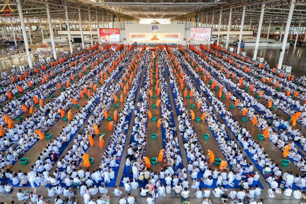 พุทธศาสนิกชนชุดขาวจำนวนมากนั่งเรียงแถวตักบาตรพระภิกษุสงฆ์ภายในอาคารสภาธรรมกายสากล
