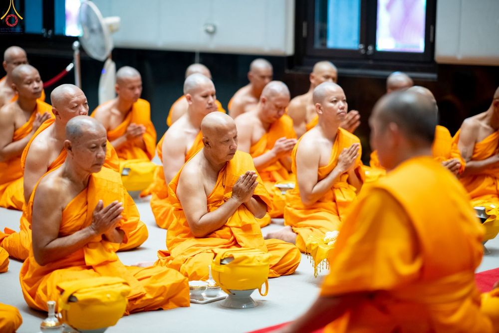 พระภิกษุสงฆ์หลายรูปนั่งพนมมือประกอบพิธีกรรมทางศาสนาภายในอาคาร