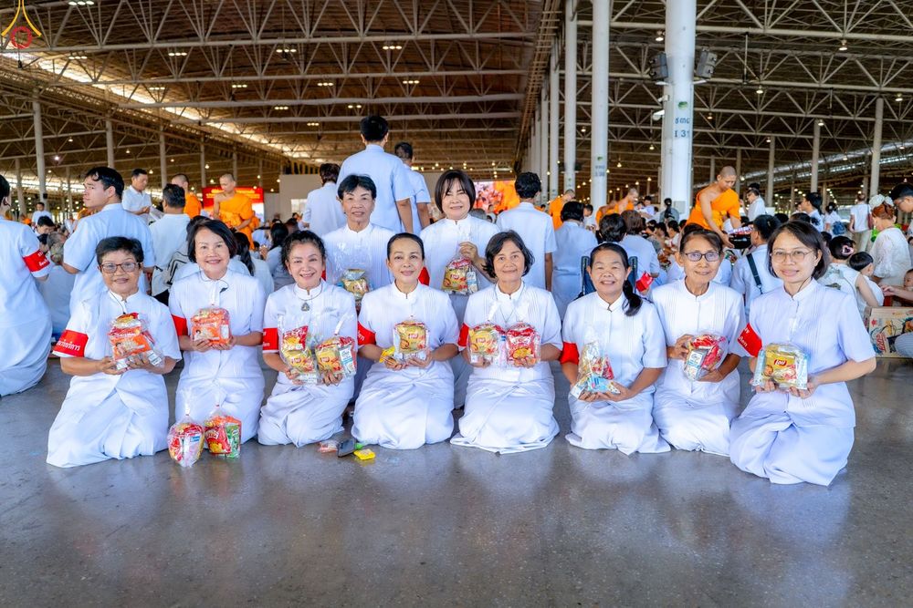 กลุ่มผู้หญิงสวมชุดขาวนั่งถือถุงอาหารแห้งเตรียมตักบาตรภายในสภาธรรมกายสากล