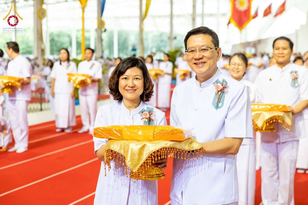 ชายและหญิงสวมชุดสีขาวถือพานผ้าไตรจีวรในพิธีทอดผ้าป่า