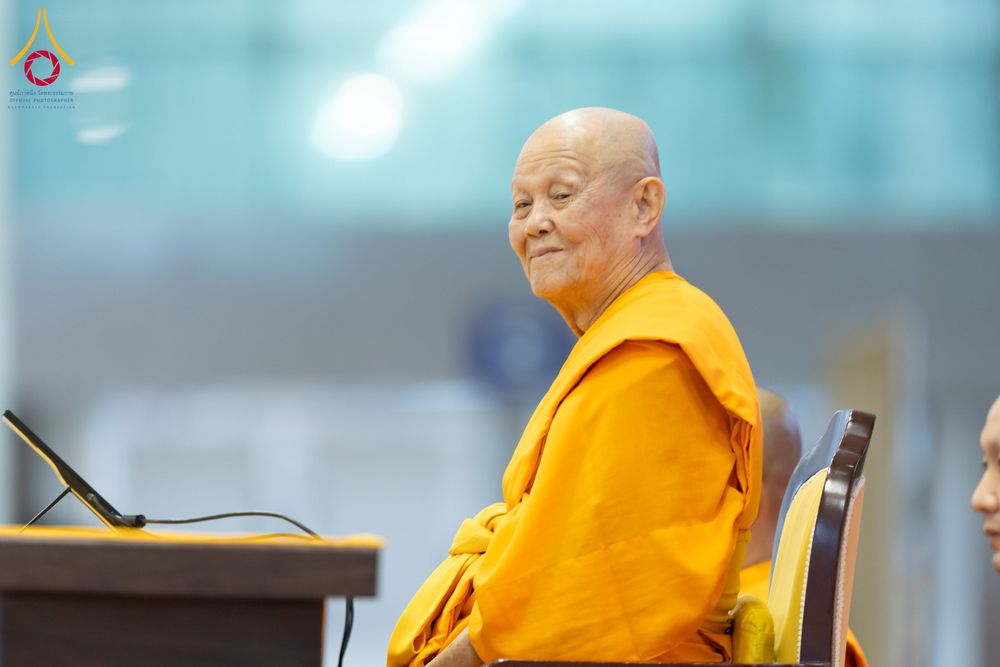พระภิกษุสงฆ์ครองจีวรสีเหลืองทองนั่งอยู่บนเก้าอี้ในอาคารสภาธรรมกายสากล