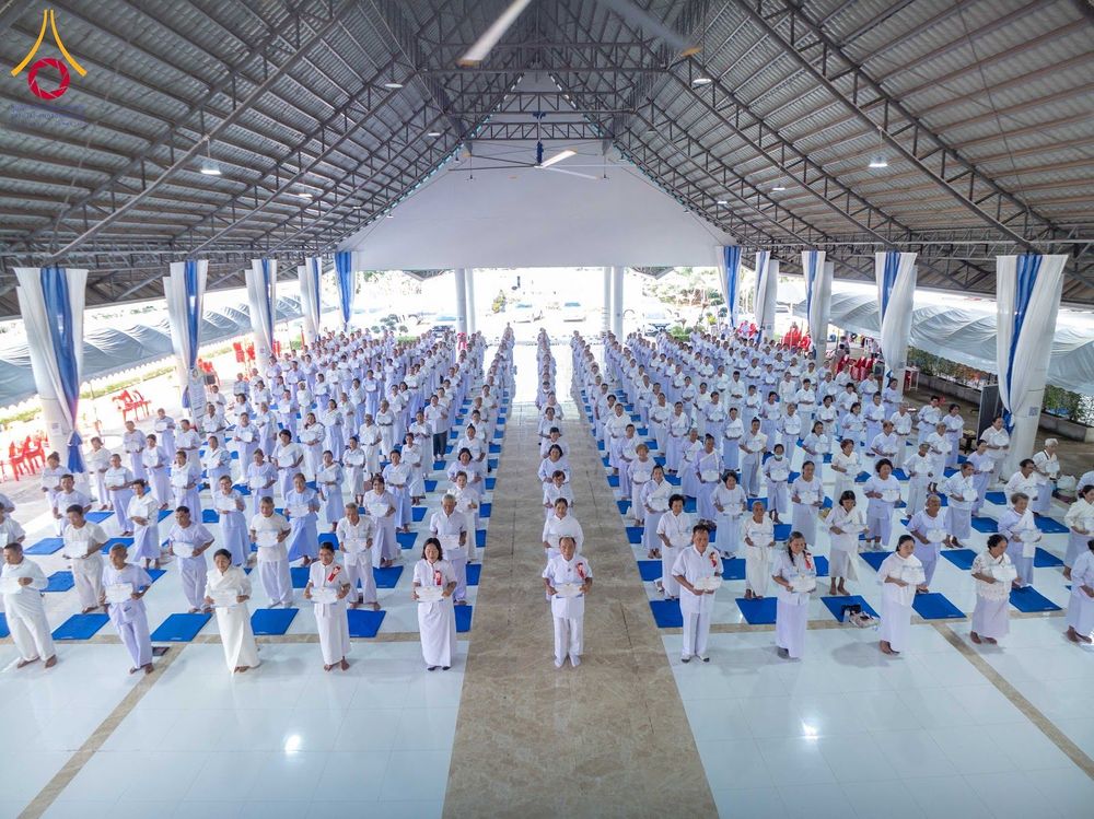 กลุ่มผู้เข้าร่วมโครงการอบรมอุบาสกแก้วและอุบาสิกาแก้วสวมชุดสีขาว ยืนเรียงแถวอย่างเป็นระเบียบภายในอาคารปฏิบัติธรรม