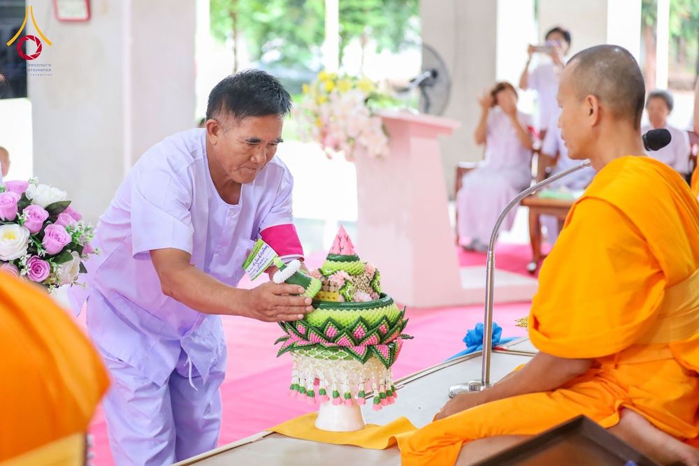 อุบาสกสวมชุดขาวกำลังถวายพานพุ่มดอกไม้ให้แก่พระภิกษุสงฆ์ในงานพิธี