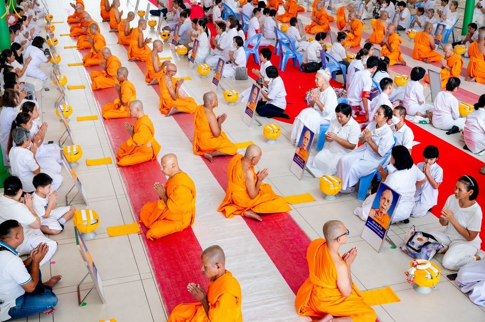 กลุ่มพระภิกษุและพุทธศาสนิกชนนั่งพนมมือประกอบพิธีทางศาสนาภายในอาคาร