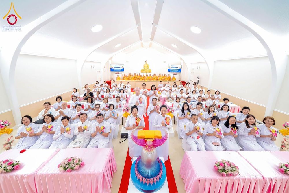 กลุ่มพุทธศาสนิกชนในชุดสีขาวนั่งร่วมพิธีทอดผ้าป่าภายในห้องโถงวัดที่มีพระภิกษุสงฆ์เป็นประธาน