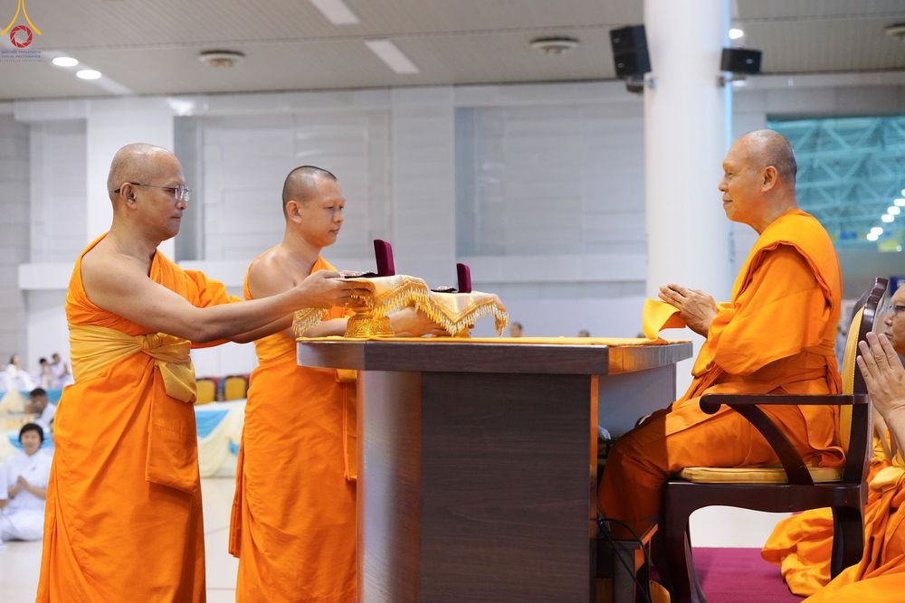 พระภิกษุสงฆ์ในจีวรสีส้มกำลังทำพิธีมอบพระของขวัญให้แก่พระภิกษุอีกรูปหนึ่งภายในอาคาร