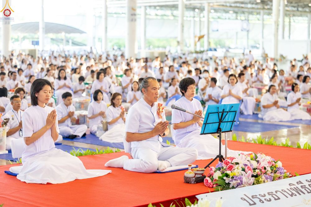 พุทธศาสนิกชนสวมชุดขาวนั่งพนมมือร่วมพิธีตักบาตรภายในอาคารสภาธรรมกายสากล