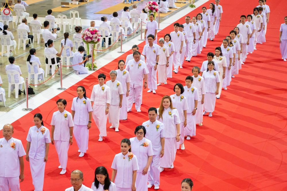 กลุ่มคนในชุดสีขาวเดินแถวเรียงเดี่ยวบนพรมสีแดงภายในอาคาร