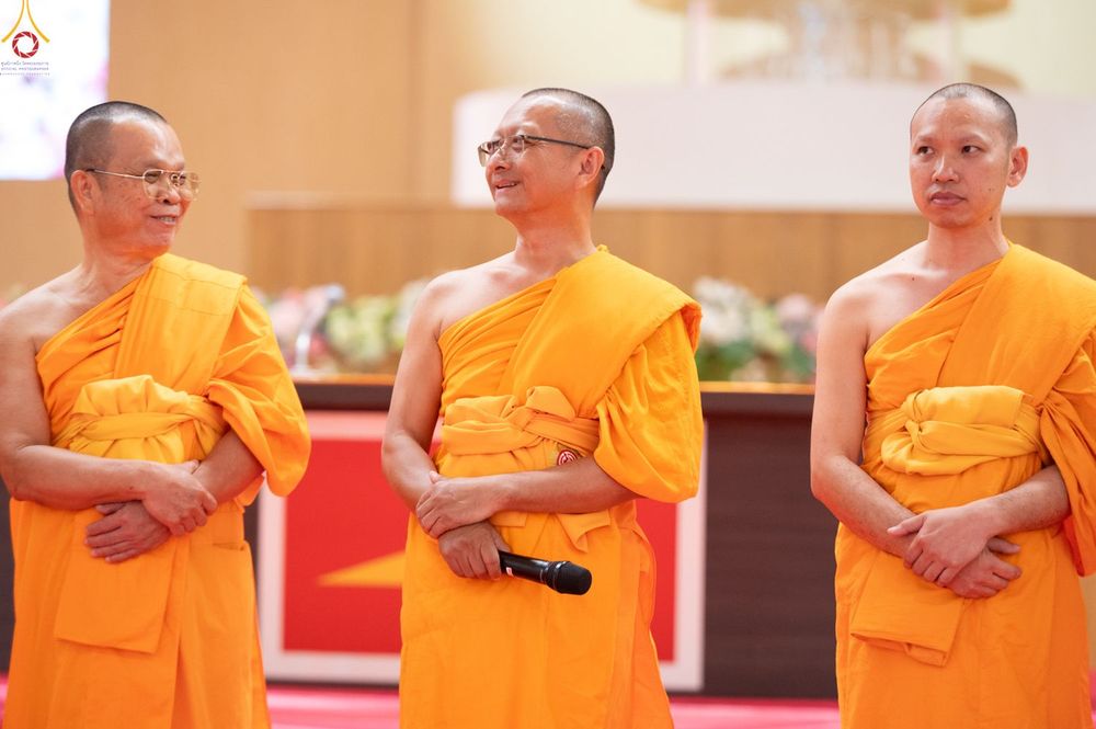 พระภิกษุสงฆ์สามรูปครองจีวรสีเหลืองทองยืนอยู่บนเวทีในงานสัมมนา