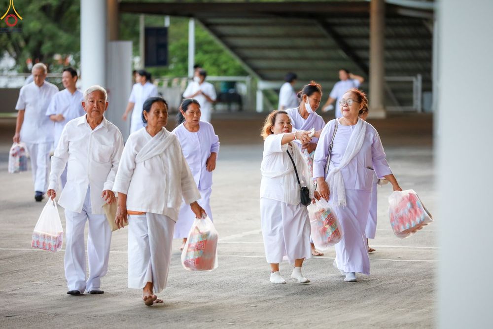 กลุ่มคนสวมชุดสีขาวถือถุงอาหารแห้งเดินในพื้นที่วัด