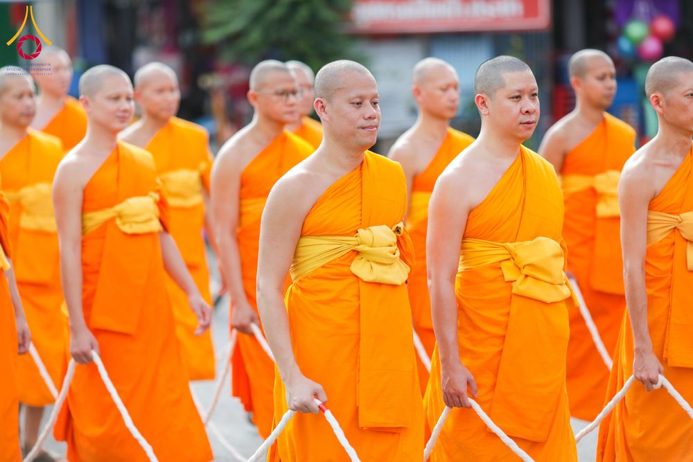 พระภิกษุสงฆ์หลายรูปสวมจีวรสีส้มเดินแถวถือสายสิญจน์ในพิธีทางศาสนา