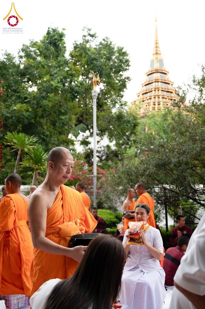 พระภิกษุและสามเณรในจีวรสีส้มกำลังรับบิณฑบาตจากประชาชนที่มาทำบุญในวัด