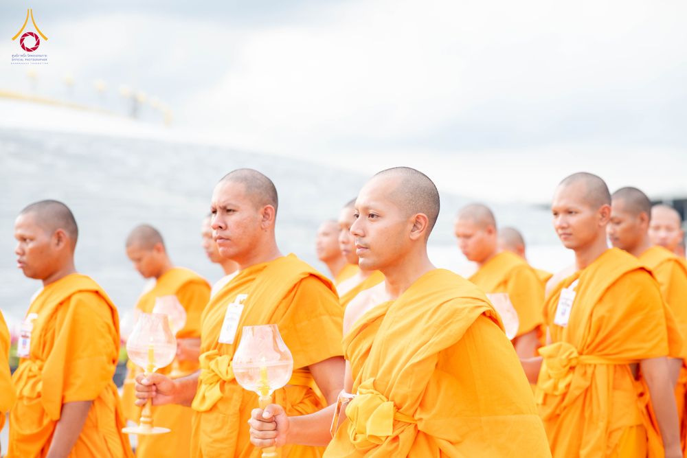 พระภิกษุสงฆ์หลายรูปยืนเรียงแถวถือโคมประทีปแก้วในมือ