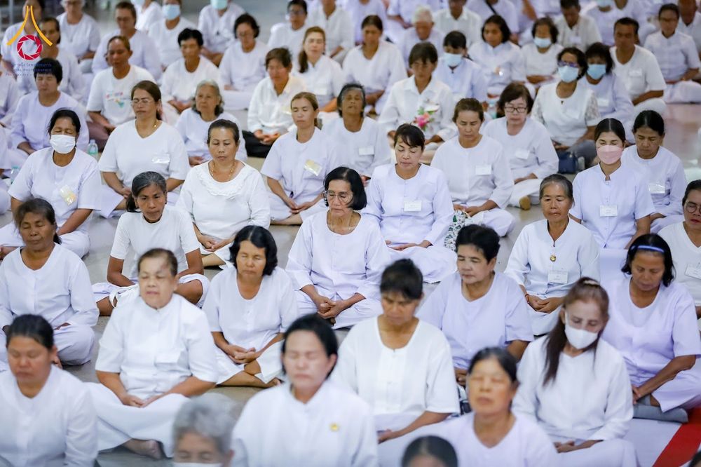 กลุ่มอุบาสิกาแก้วสวมชุดสีขาวนั่งสมาธิเรียงแถวกันอย่างเป็นระเบียบภายในศูนย์อบรม