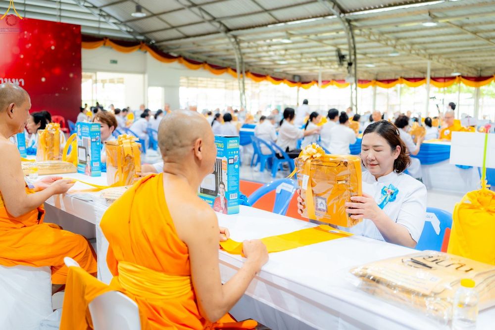 หญิงสาวกำลังประเคนชุดสังฆทานให้พระภิกษุสงฆ์ในงานบุญที่มีผู้คนมาร่วมงานจำนวนมาก