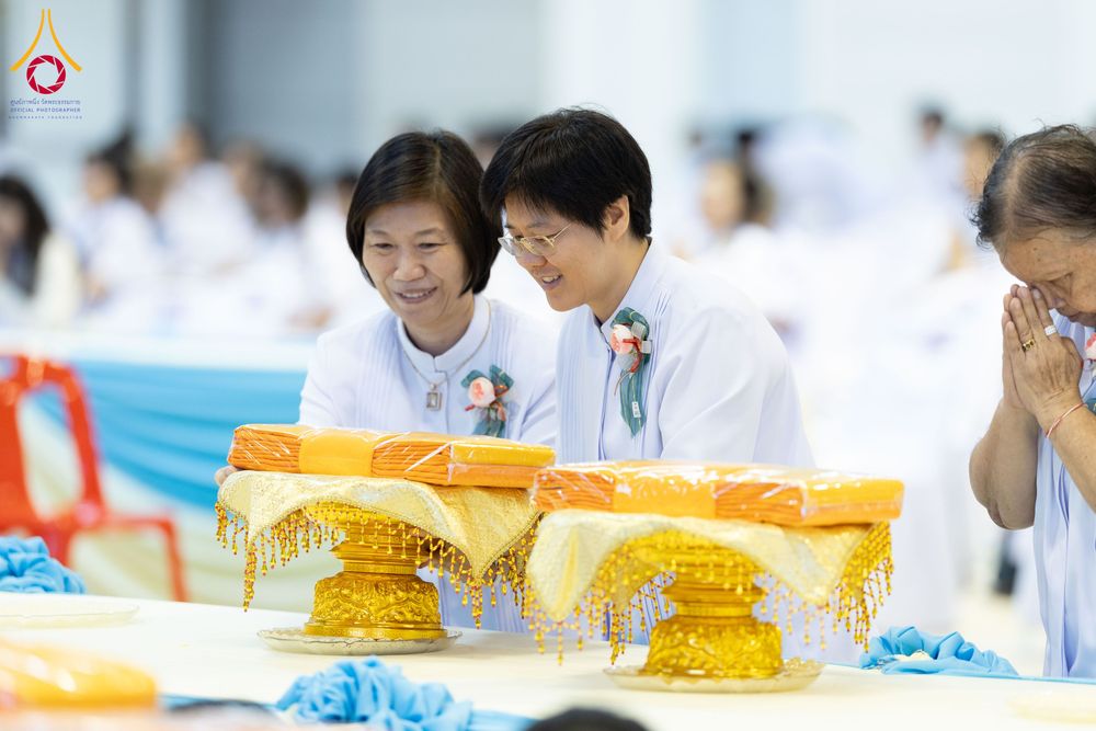 ผู้หญิงสองคนสวมชุดสีขาวกำลังจัดเตรียมผ้าไตรบนพานทองในพิธีทางศาสนา