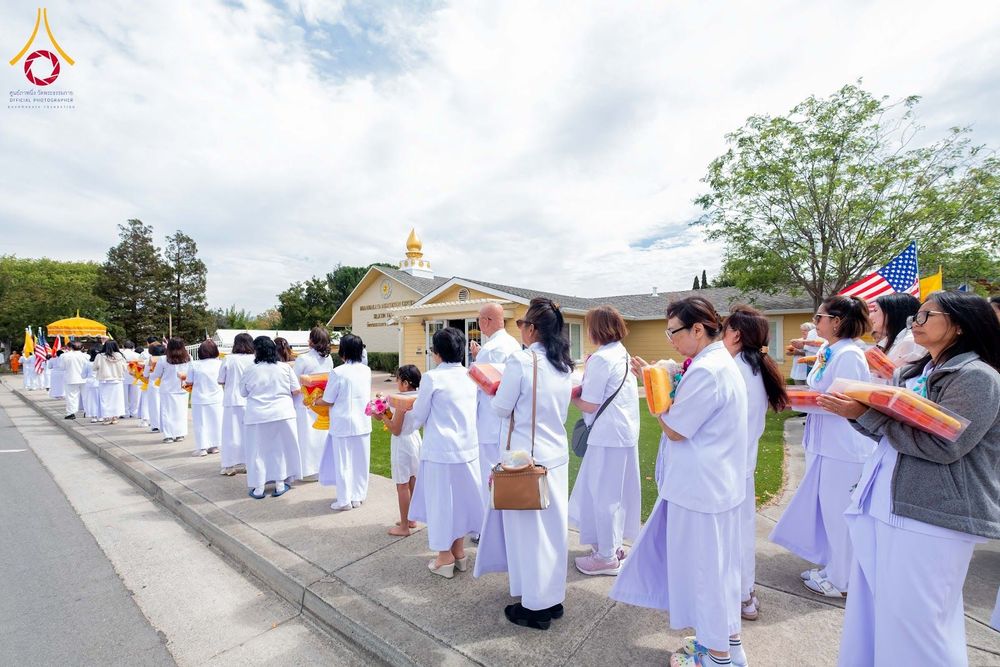 กลุ่มคนสวมชุดสีขาวถือผ้าไตรเดินเป็นแถวหน้าอาคารวัดพระธรรมกายซิลิคอนวัลเลย์