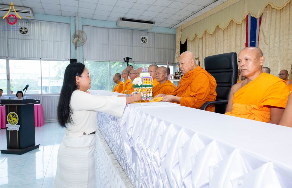 หญิงสวมชุดสีขาวกำลังประเคนพานพุ่มบรรจุพระบรมสารีริกธาตุแด่พระภิกษุสงฆ์ภายในอาคาร