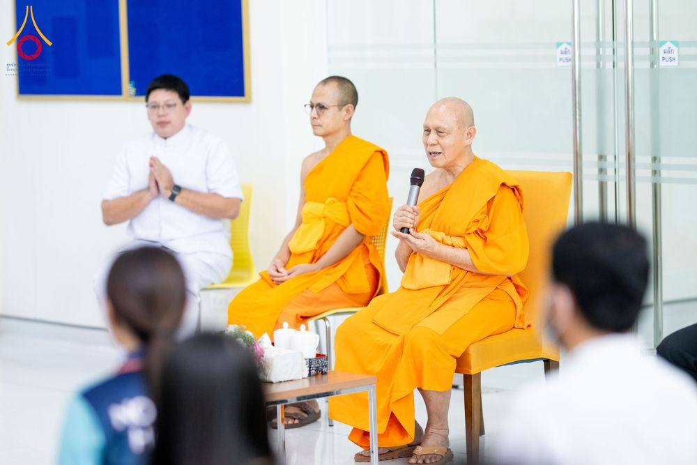 พระสงฆ์กำลังพูดผ่านไมโครโฟนท่ามกลางผู้เข้าร่วมกิจกรรมในอาคาร