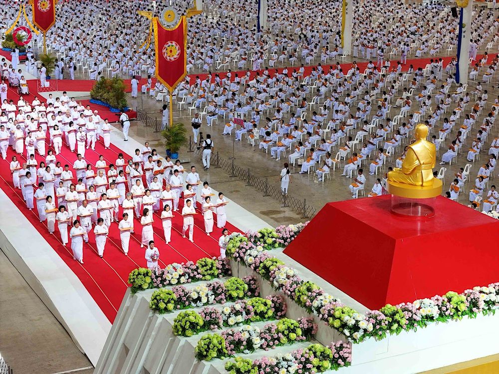พุทธศาสนิกชนชุดขาวเดินแถวบนพรมแดงในพิธีทอดผ้าป่าภายในสภาธรรมกายสากล