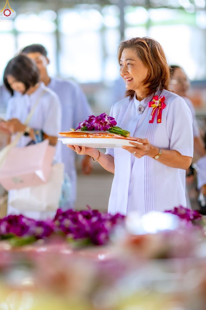 หญิงไทยสวมชุดสีขาวถือถาดอาหารแห้งและดอกไม้ในพิธีตักบาตร