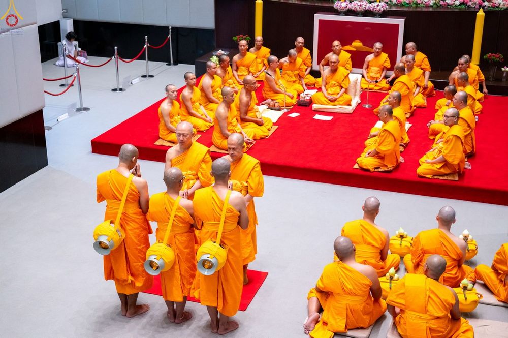 กลุ่มพระภิกษุและผู้เข้าร่วมพิธีอุปสมบทในชุดจีวรสีเหลืองทองนั่งบนพรมสีแดงภายในอาคาร